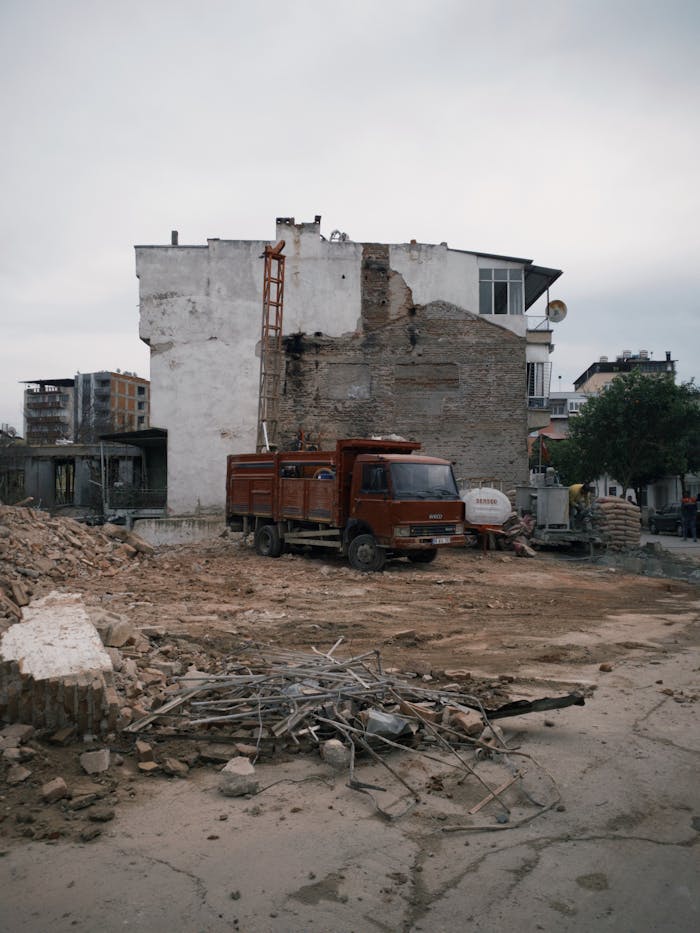 A city demolition site featuring a red truck, debris, and partially demolished buildings.